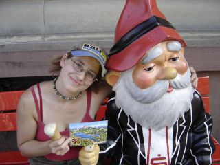 Jenny sitzt neben einer Zwergenfigur, h�lt eine Postkarte und ein Eis in den H�nden